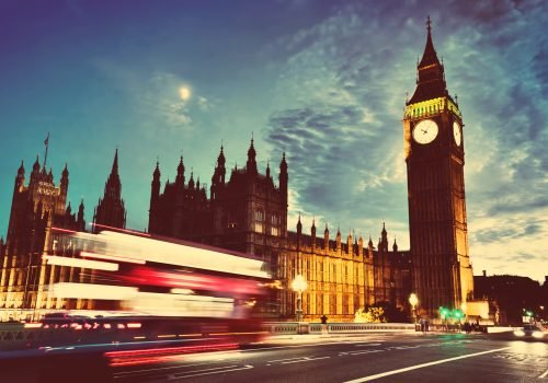 Red bus in motion, Big Ben and Westminster Palace in London, the UK. at night. View from Westminster Bridge. Moon shining, vintage, retro.
